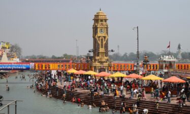 Vibrant scene of pilgrims bathing in Haridwar's Ganges with the iconic clock tower in view.