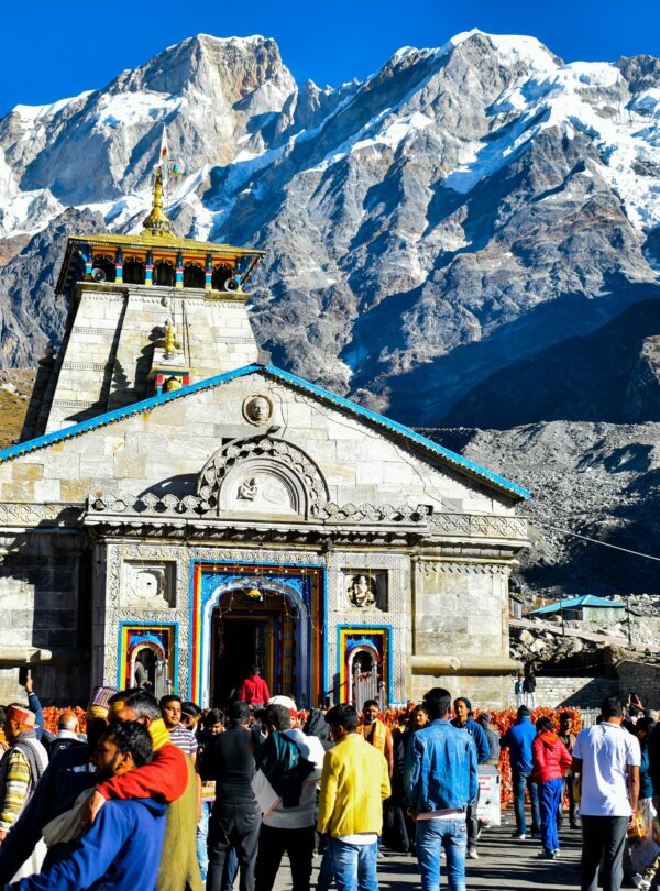 Crowd gathers at Kedarnath Temple with Himalayas backdrop, showcasing religious significance and stunning landscape.