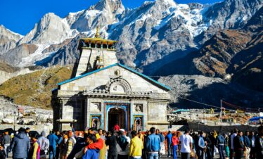 Crowd gathers at Kedarnath Temple with Himalayas backdrop, showcasing religious significance and stunning landscape.