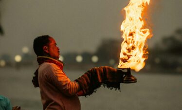 A man in traditional attire performs a fire ritual by the Ganges River in Rishikesh, India.