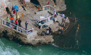 Aerial view of people performing rituals by the river in Rishikesh, India. The turquoise waters add a serene beauty.